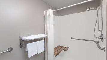 Un baño moderno con ducha, barras de apoyo, perchero y repisa de madera.
