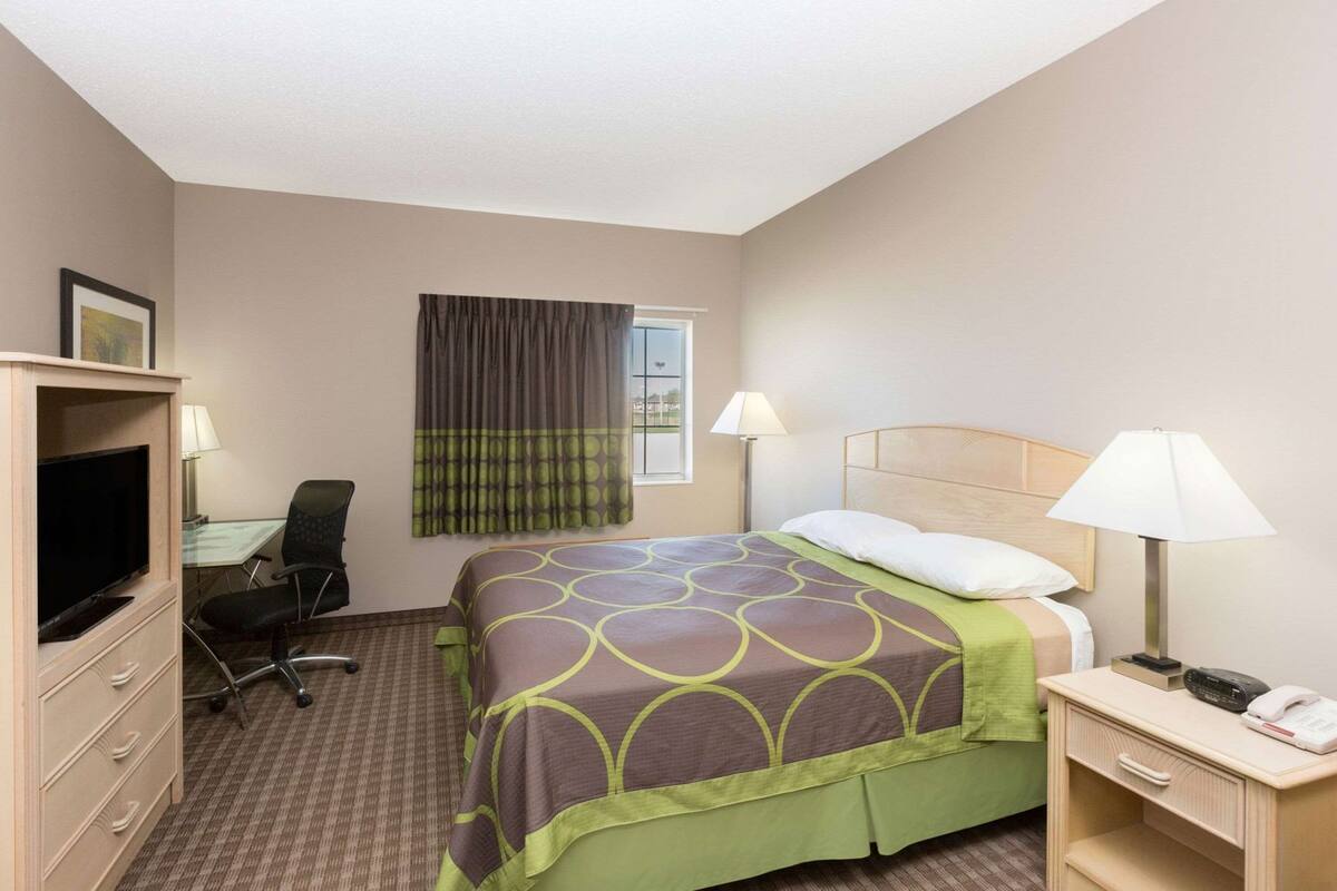 A hotel room with a bed, desk, chair, television, lamps, and a telephone.