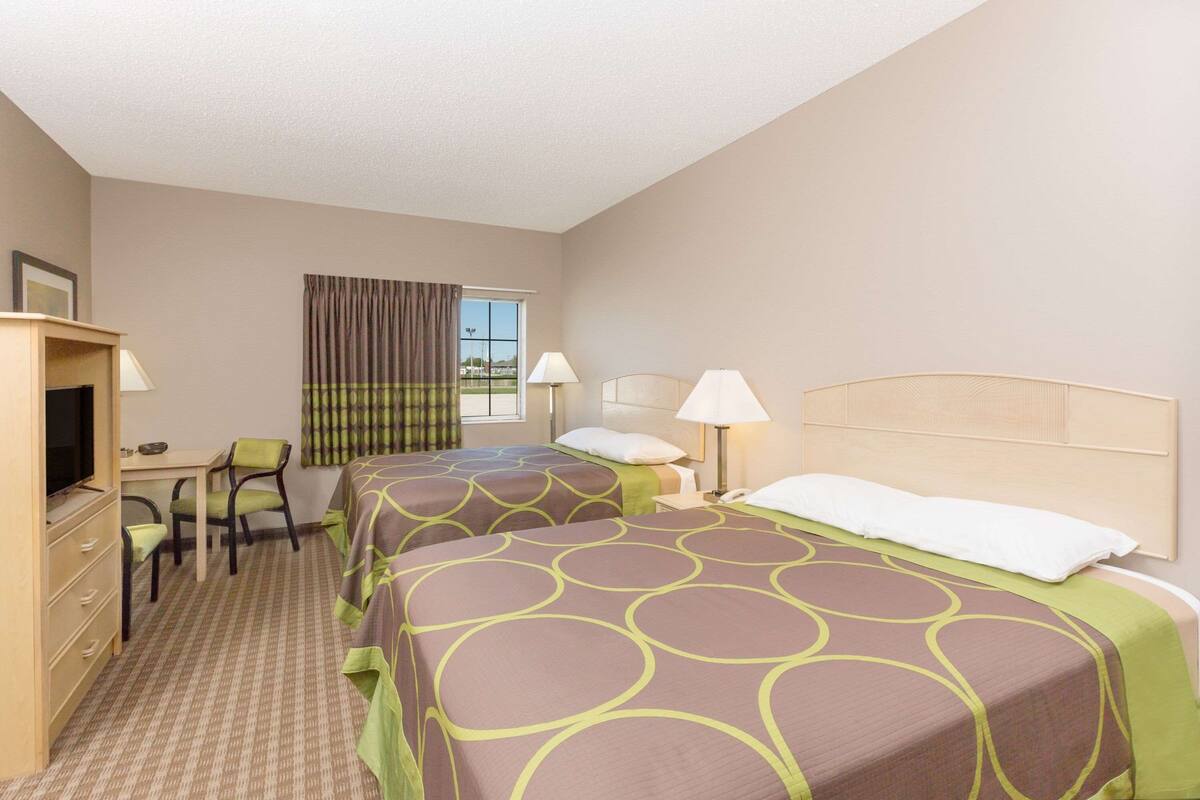 A hotel room with two beds, a desk, a chair, and a television.