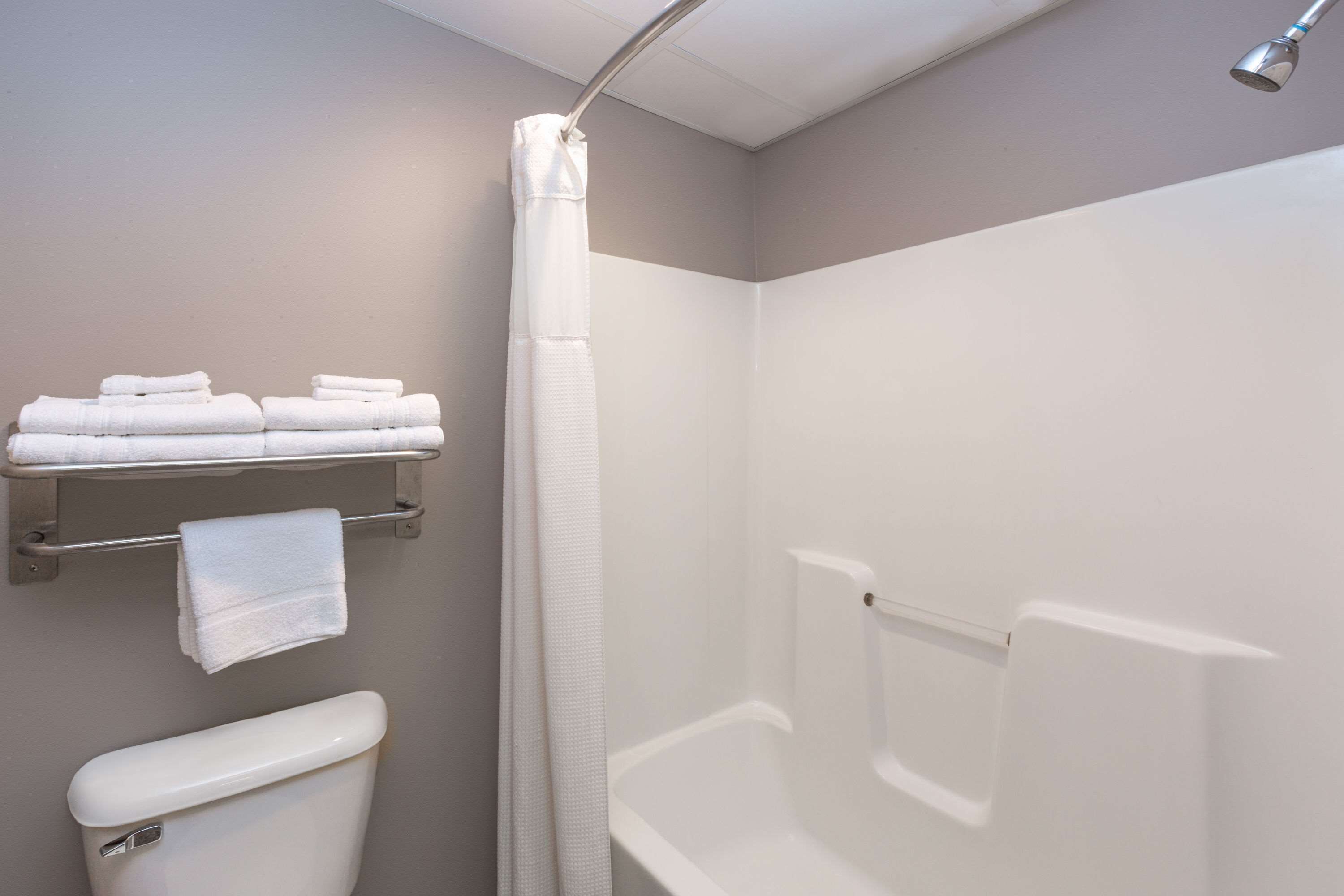 A bathroom with a toilet, a shower, and a towel rack with folded towels.