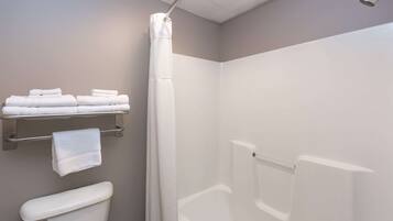 A bathroom with a toilet, a shower, and a towel rack with folded towels.