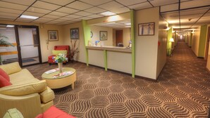 Eine Hotelhalle mit Rezeption, einer Wartezone inklusive Sofa und Sesseln, sowie einem gemusterten Teppich.