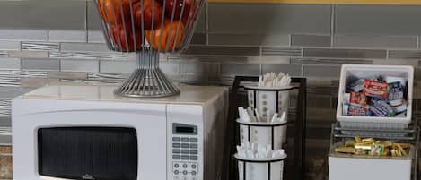 A kitchen with a white microwave, a fruit basket, a coffee maker, and a storage container.