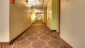 Ein Hotel-Flur mit gemustertem Teppich, hellgrünen Wänden und einer Decke mit eingelassenen Leuchten.