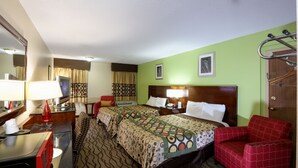 Ein Hotelzimmer mit zwei Betten, einem Schreibtisch mit Lampe, einem Stuhl, einer Kommode und einer Tür mit Griff.
