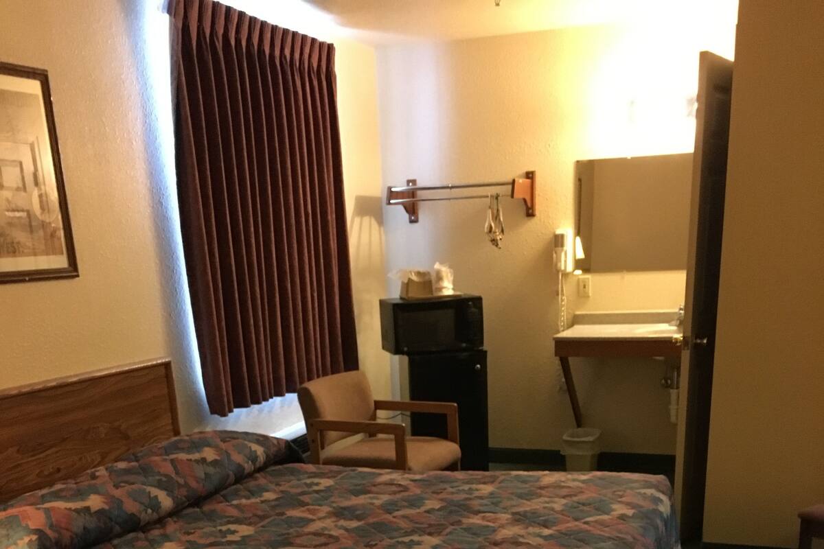 A hotel room with two beds, a chair, a TV, a small table, and a bathroom area.