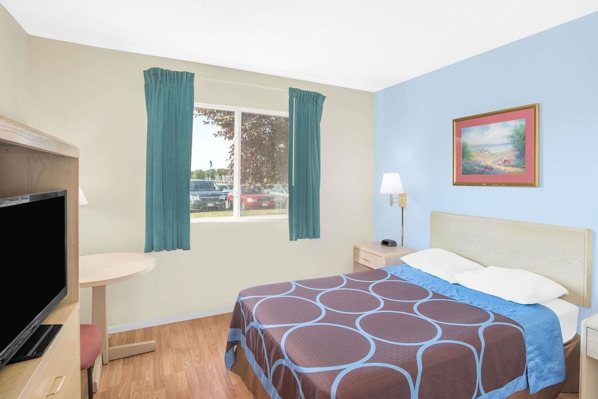 A hotel room with a bed, a TV, a desk, a lamp, and a window with curtains.