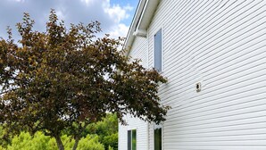 A white building with a tree in front, a picnic table, and a lamp on the wall. - Super 8 by Wyndham Canandaigua (Canandaigua)