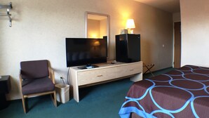 Una habitación de hotel con una cama, televisión, escritorio con lámpara, silla y un cubo de basura.