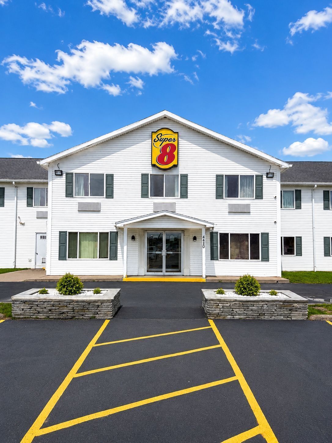 Un hôtel à deux étages, reconnaissable à son grand panneau « Super 8 », doté d’une entrée centrale et d’un parking avec des places délimitées.