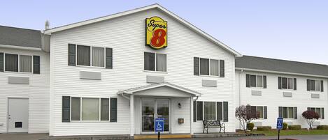 Um motel Super 8 com fachada branca, entrada central e sinalização de vagas para deficientes.