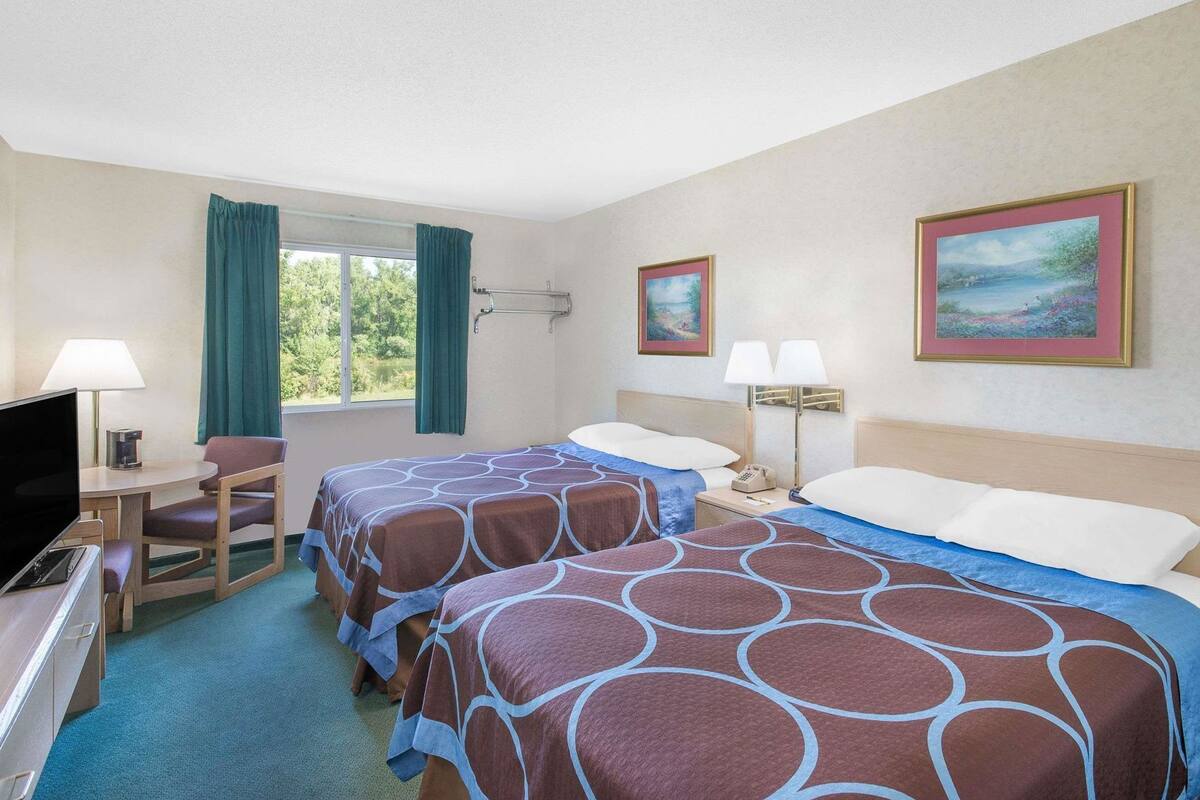 A hotel room with two beds, a desk with a TV, a chair, and a window with curtains.