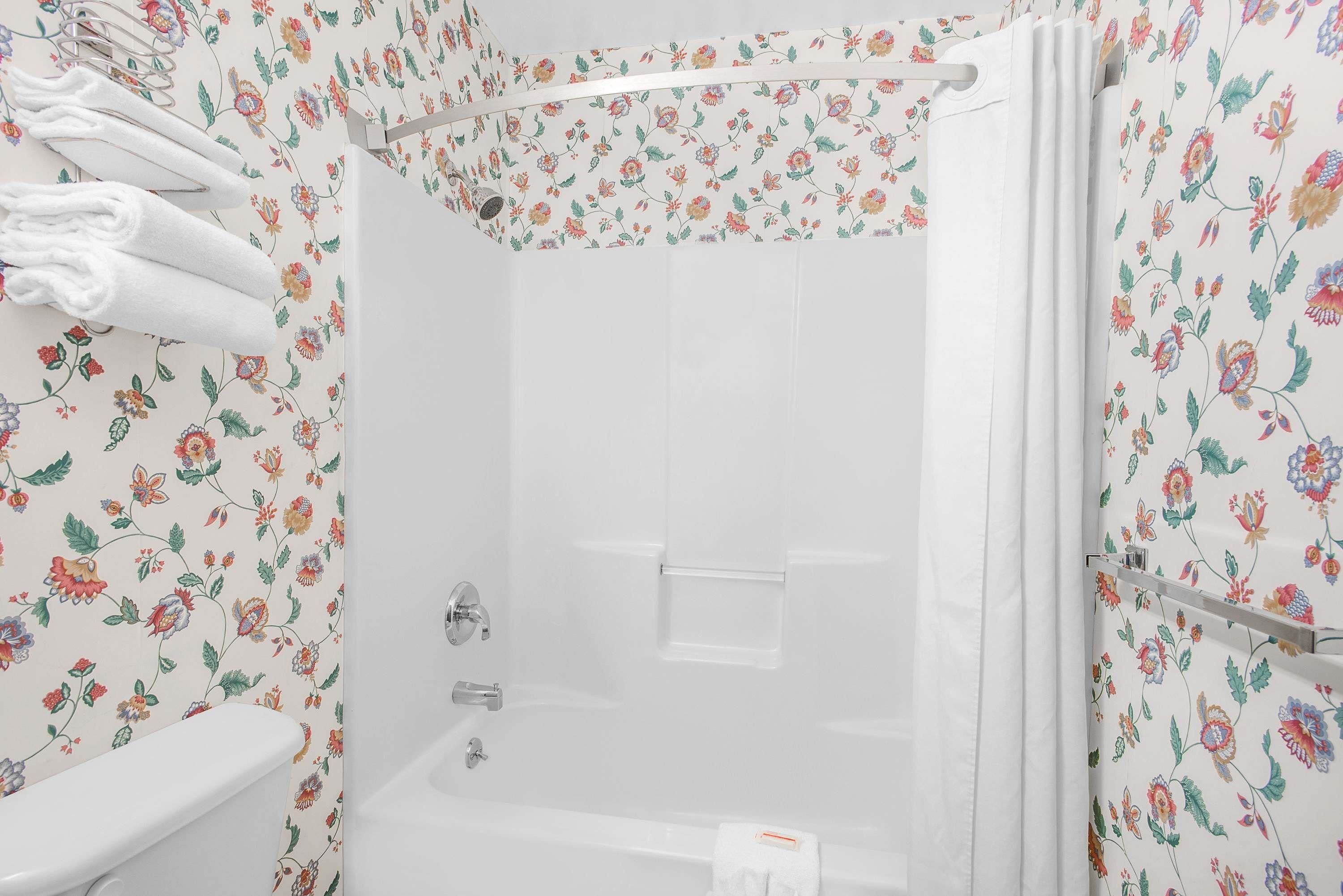 A shower with a floral wallpaper pattern, a white bathtub, and a toilet.