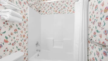 A shower with a floral wallpaper pattern, a white bathtub, and a toilet.
