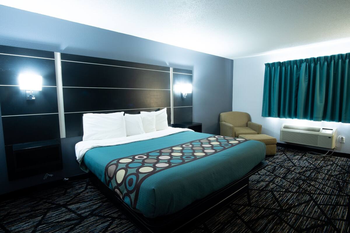 A hotel room with a bed, a chair, a nightstand, and a window with curtains.
