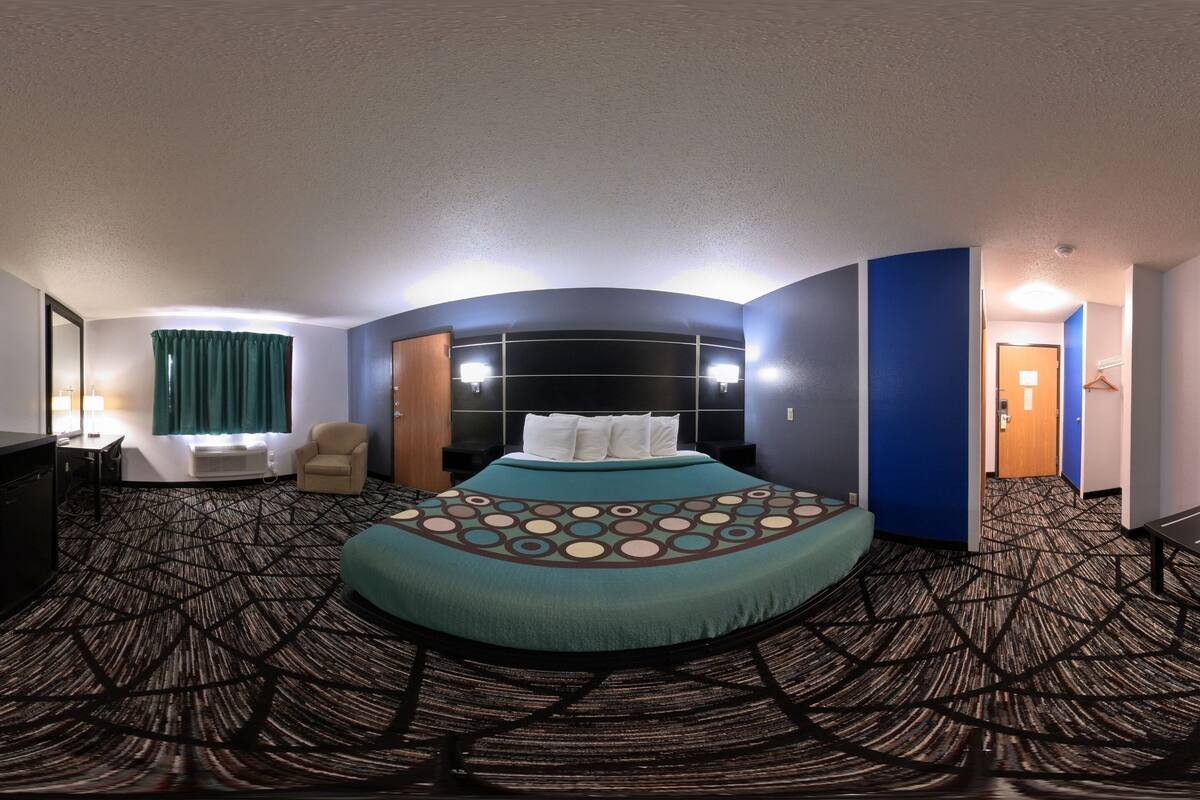 A hotel room with a large bed, a desk, a chair, and a small table.