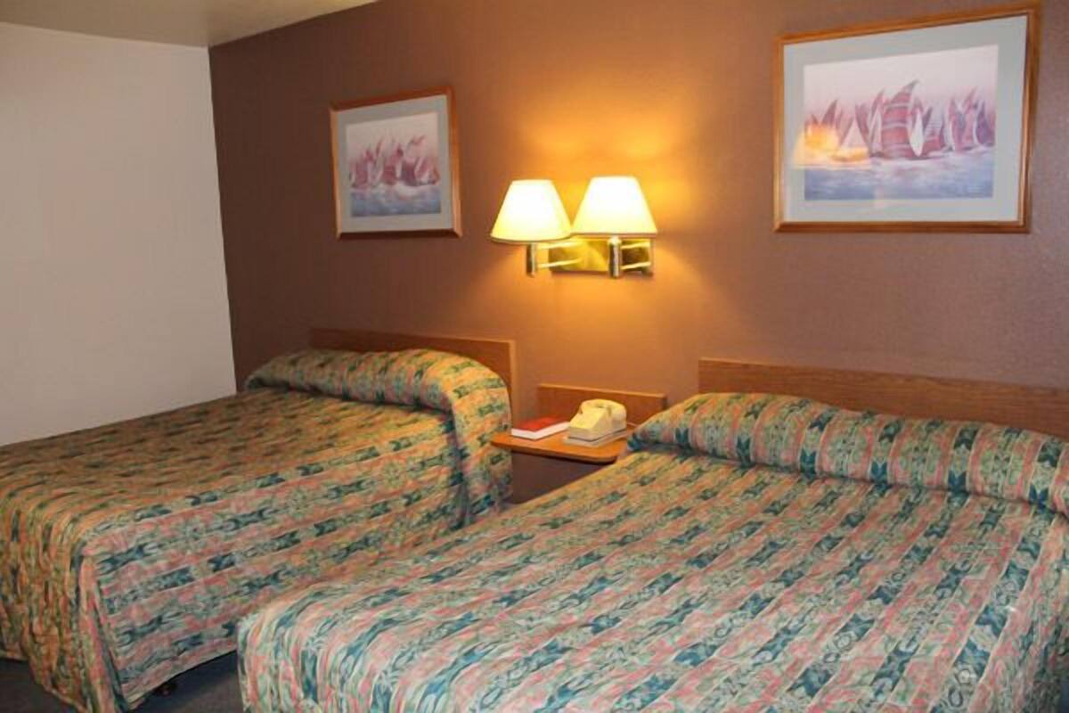 A hotel room with two beds, each with patterned bedding, a nightstand with a lamp, and framed artwork on the walls.