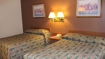 Una habitación de hotel con dos camas, cada una con ropa de cama estampada, una mesita de noche con lámpara y obras de arte enmarcadas en las paredes.