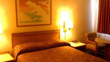 A hotel room with a bed, two bedside lamps, a chair, a small table, and a painting on the wall.