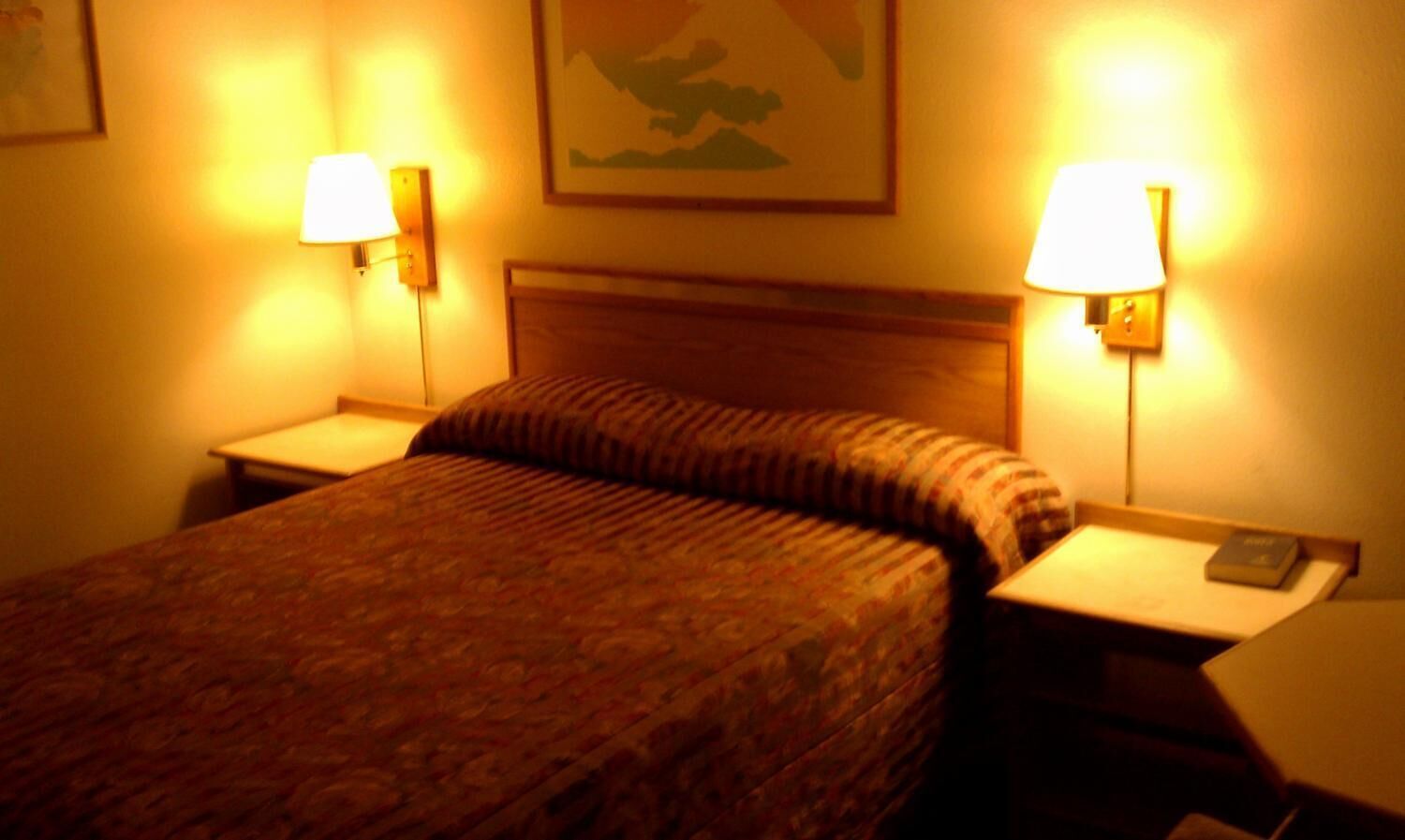 A hotel room with a bed, two bedside tables, and two wall-mounted lamps.