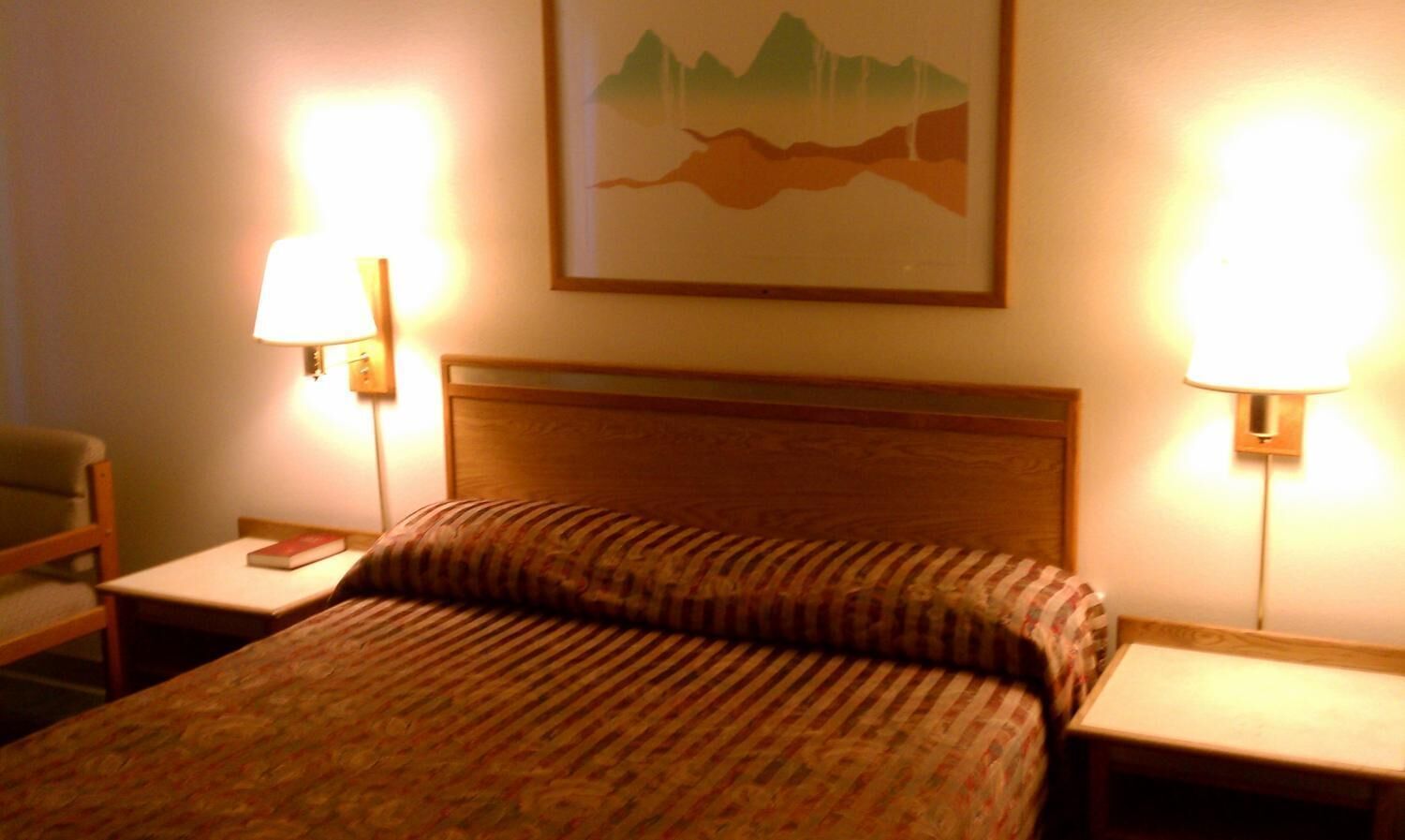 Ein Hotelzimmer mit einem Bett, zwei Nachttischen, einem Sessel und einem an der Wand hängenden Gemälde.