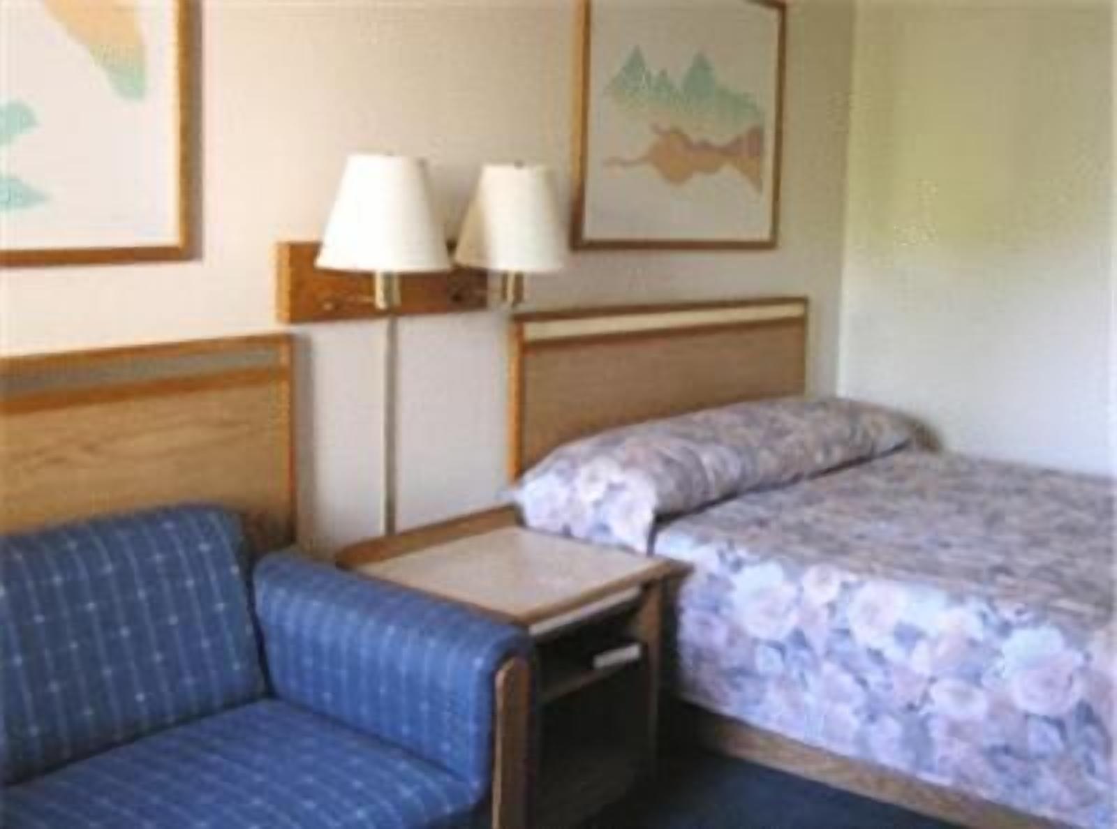 Una habitación pequeña y funcional con una cama individual, una mesita, una silla y dos lámparas fijadas a la pared.