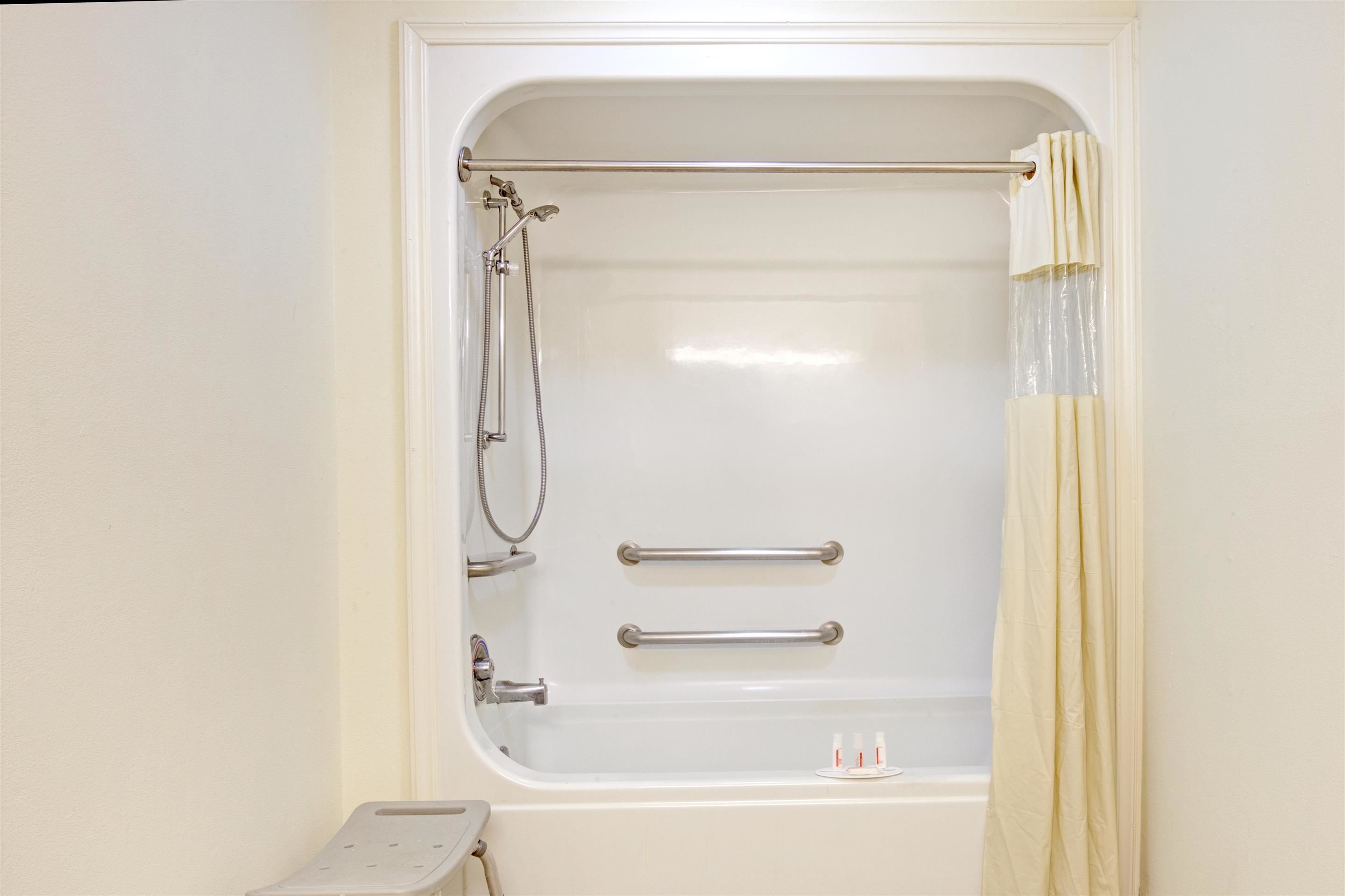 A white bathtub with a shower head, grab bars, and a curtain.