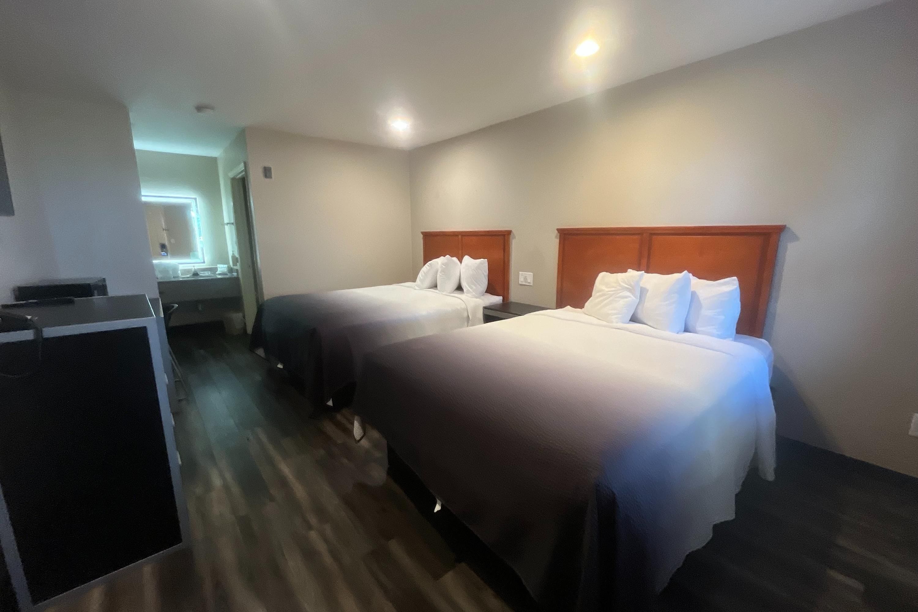 A hotel room with two beds, a desk, and a mirror.