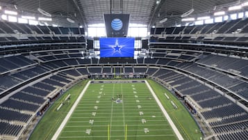 A large stadium with multiple tiers of seating, a central field marked with yard lines, and a prominent team logo on the field.
