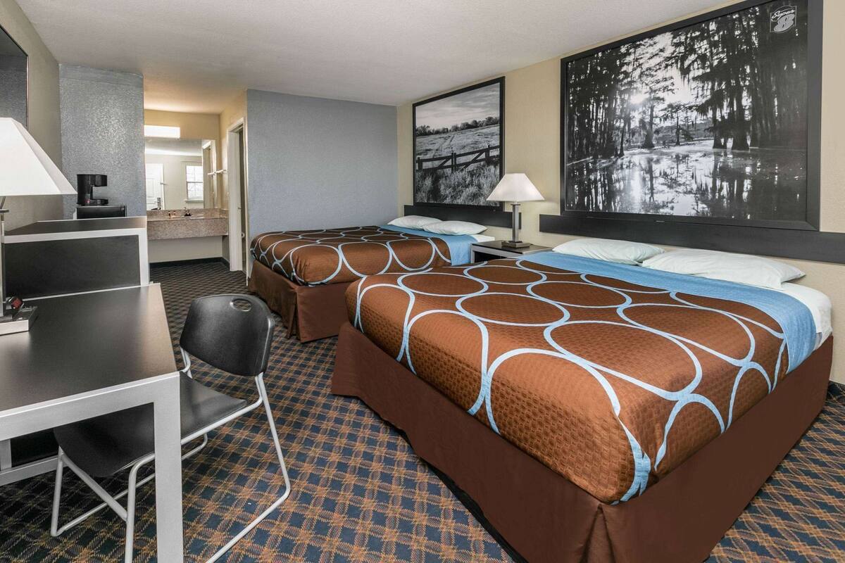 Habitación de hotel con dos camas, un escritorio, una silla, una lámpara y un cuadro grande en la pared.