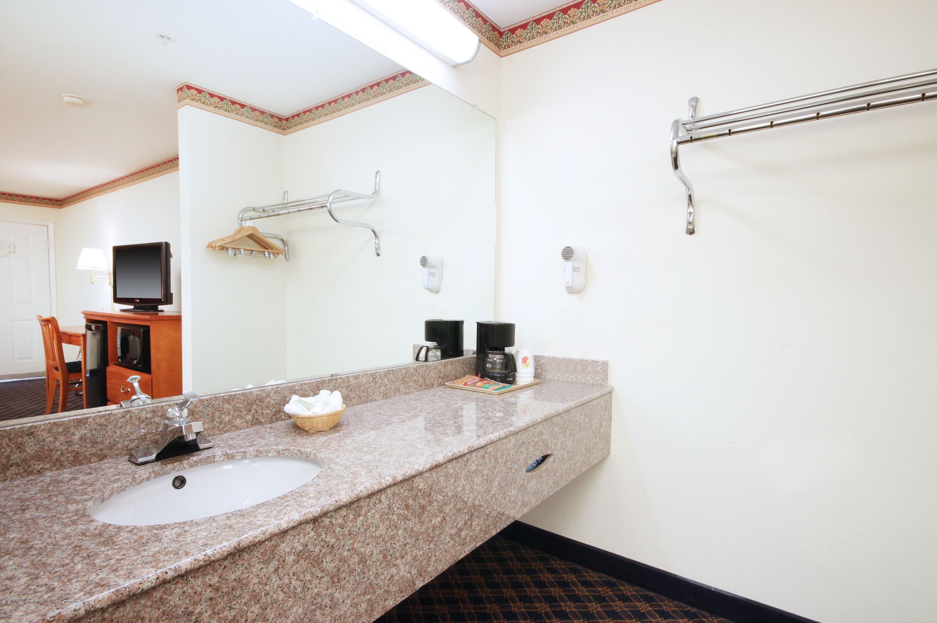 A hotel bathroom with a granite sink, a mirror, a towel rack, a hairdryer, and a coffee maker.
