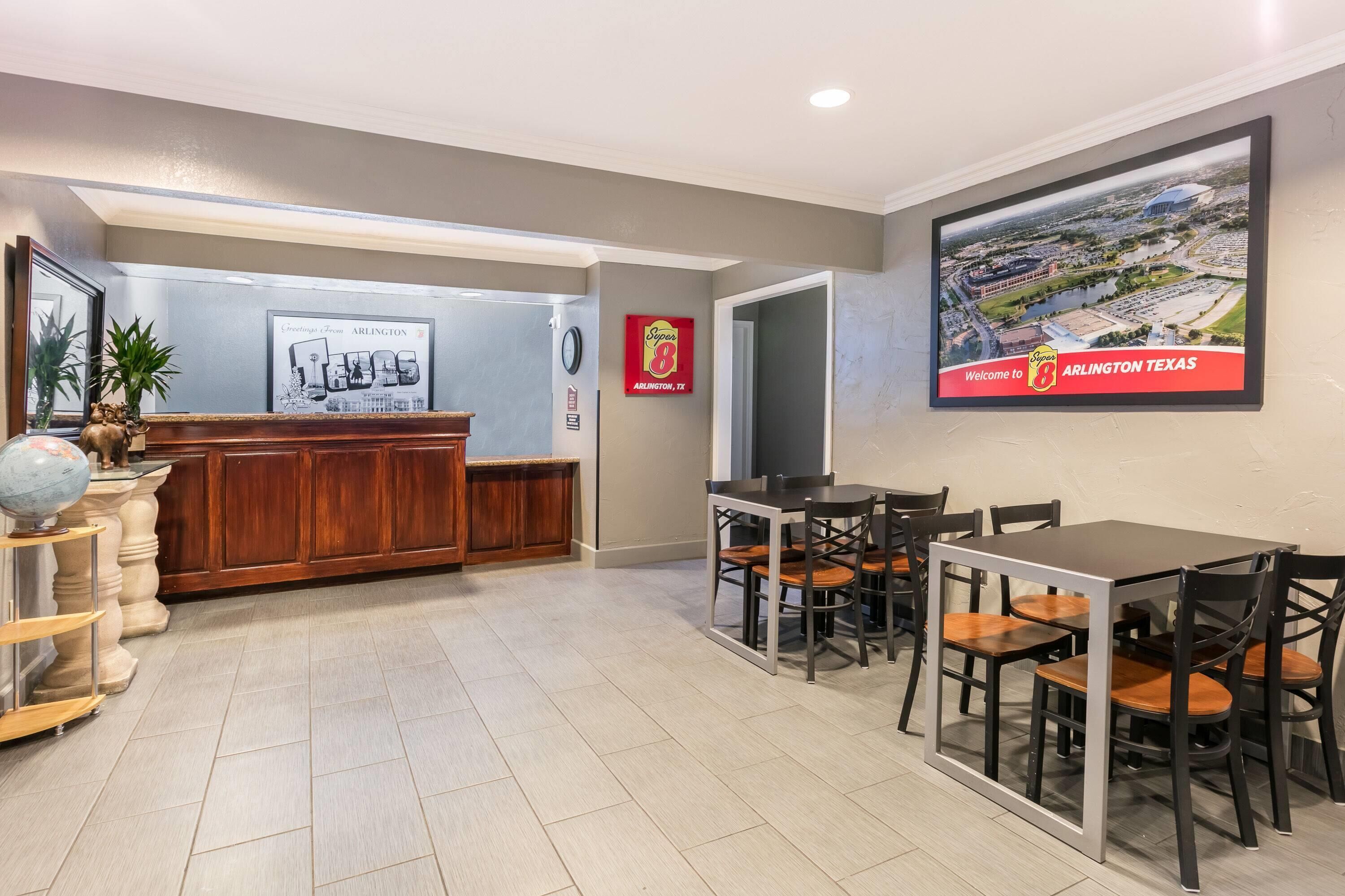 A reception area with a wooden counter, a framed welcome sign, and a dining area with tables and chairs.