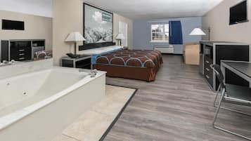 Habitación de hotel con una cama grande, baño independiente con bañera, escritorio, silla y televisor.