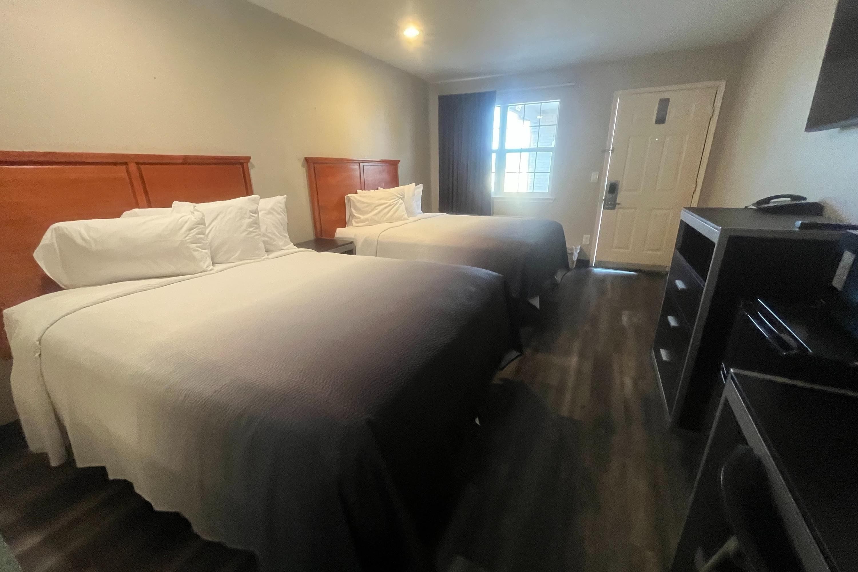 A hotel room with two beds, a desk, a dresser, and a window.
