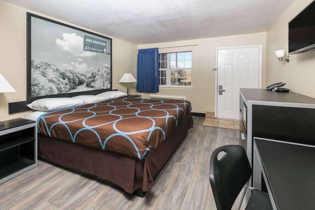 Una habitación de hotel con cama, escritorio, silla, ventana con cortinas y televisor montado en la pared.
