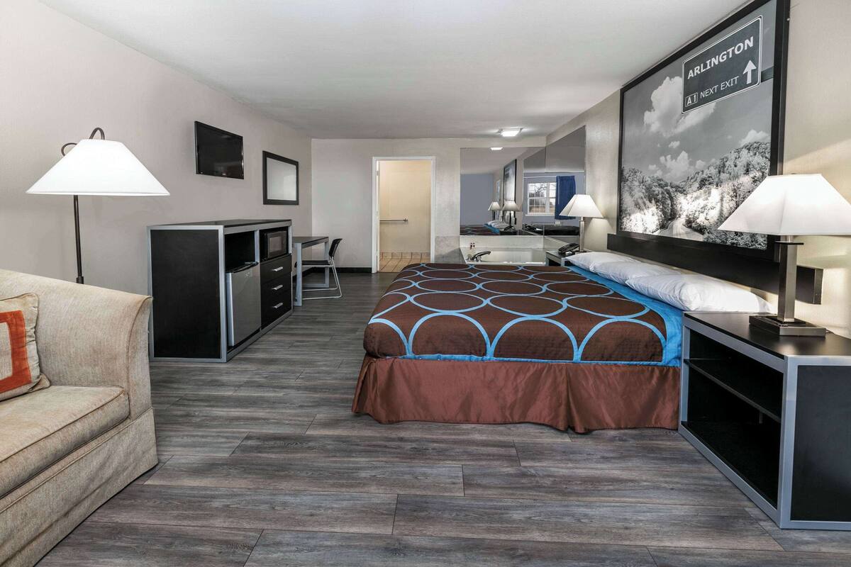 Habitación de hotel con cama, escritorio, sillón, televisor y baño visible a través de una puerta abierta.