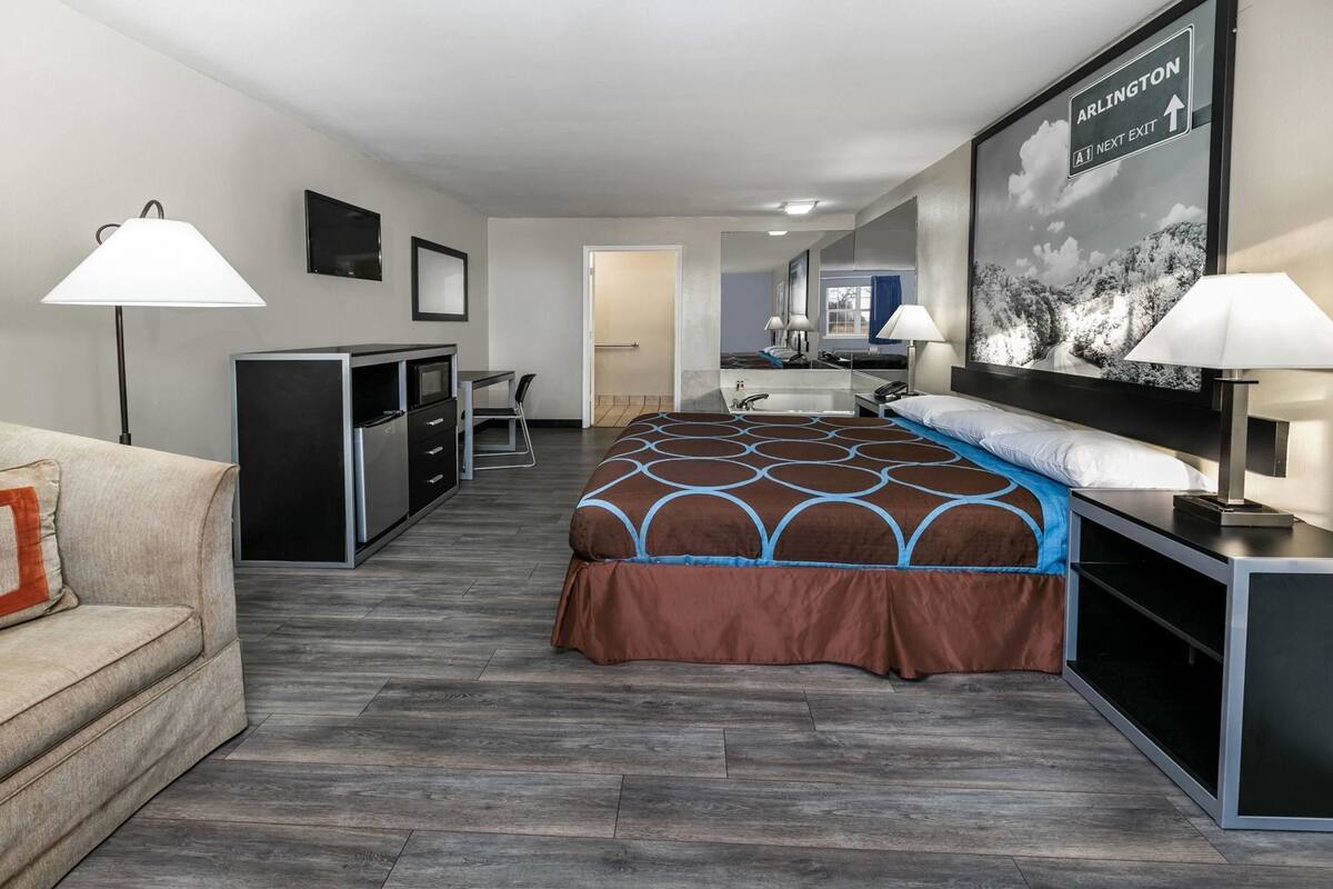 Habitación de hotel con cama, escritorio, silla, televisor y un cuadro en la pared.