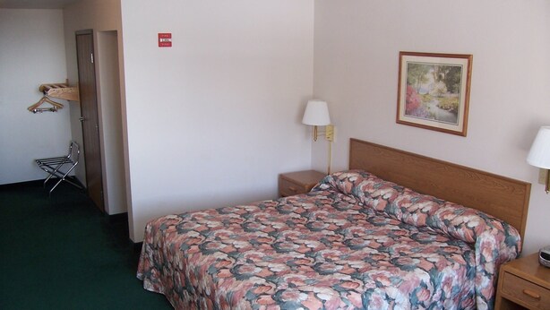 Habitación de hotel con cama, dos mesitas de noche, una lámpara, un cuadro en la pared y señal de salida de incendios.