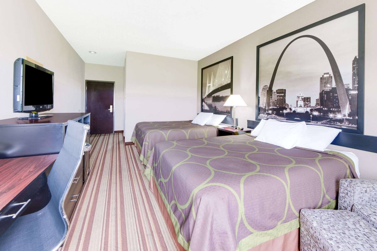 A hotel room with two beds, a desk, a TV, and a cityscape view.