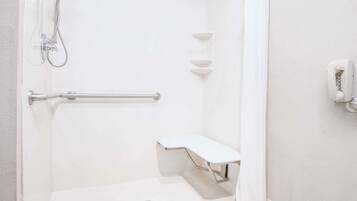 A white bathroom with a shower, a handrail, a bench, and a wall-mounted phone.