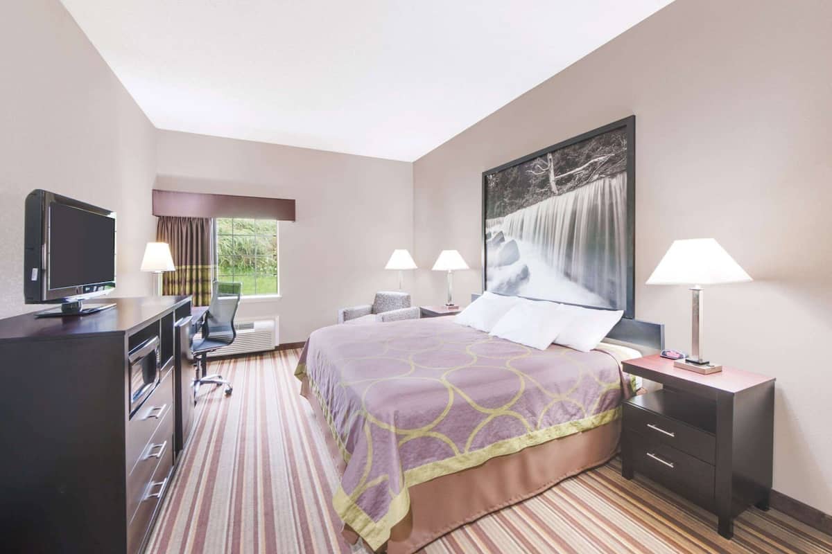 A hotel room with a bed, a desk, a TV, and a large window with curtains.