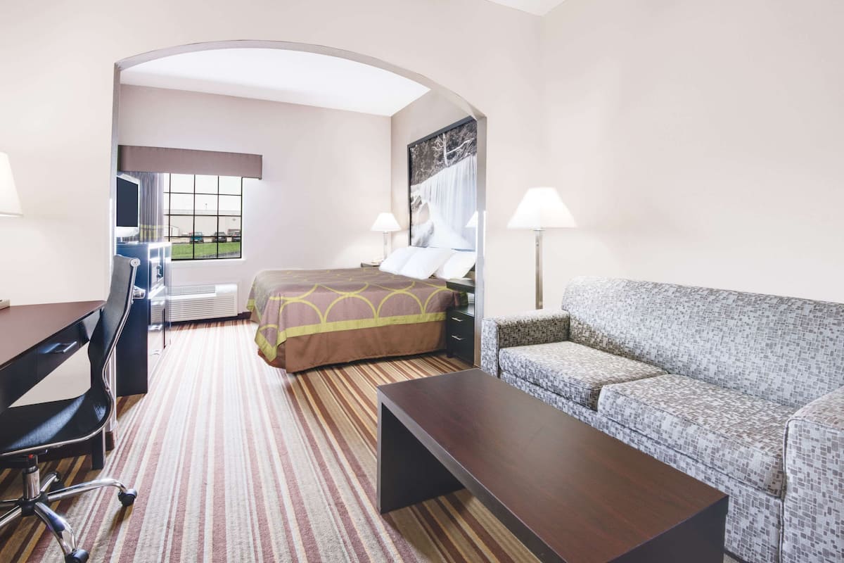 A hotel room with a bed, a sofa, a desk, and a chair. There is a window with a view of a parking lot.