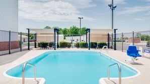 A rectangular swimming pool with metal railings, surrounded by a fence, and a covered seating area with chairs.