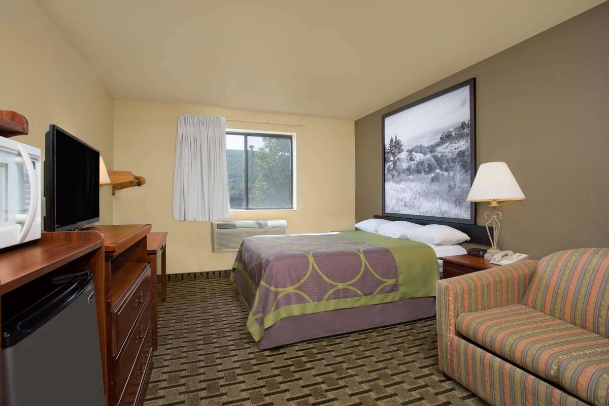 A hotel room with a bed, a TV, a desk, a chair, and a window with curtains.