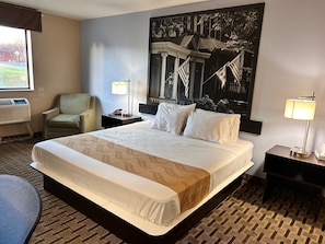 Ein Hotelzimmer mit einem großen Bett, einem Sessel, zwei Nachttischen mit Lampen, einem großen Wandbild und einer Klimaanlage.