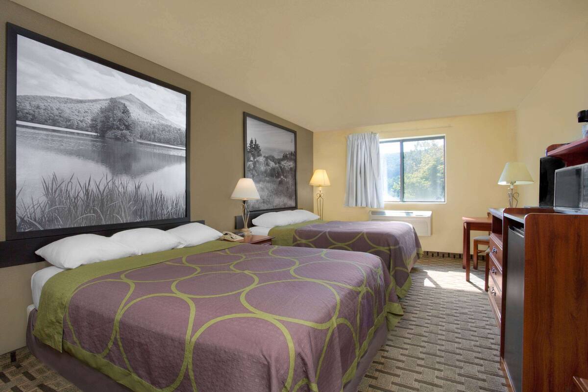 A hotel room with two beds, a desk, a chair, a TV, and large framed pictures on the walls.