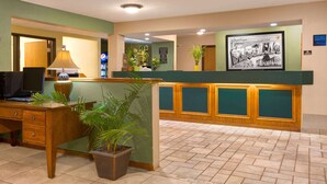 A reception area with a wooden desk, a computer, a lamp, and a potted plant. - Super 8 by Wyndham Lynchburg VA (Lynchburg)