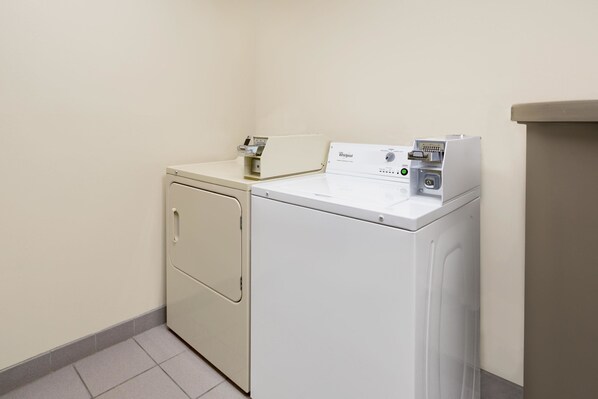 Une buanderie équipée d’un lave-linge et d’un sèche-linge à chargement frontal, d’une petite étagère avec quelques articles et d’un mur sobre.