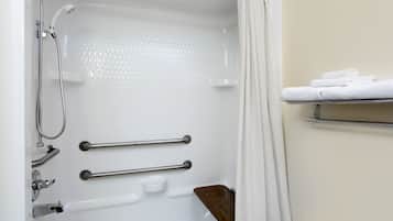A modern bathroom with a bathtub, shower, and handrails.