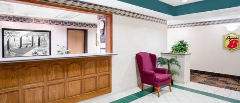 A reception area with a wooden counter, a framed welcome sign, a clock, and a Super 8 sign.